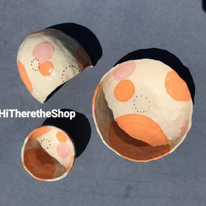 May include: Three ceramic bowls with a white background and a polka dot pattern in pink and orange. The bowls are of different sizes and are arranged in a row on a blue surface. The text "HiThereTheShop" is visible in the lower left corner of the image.