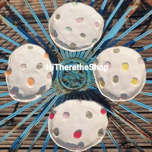 May include: Four white ceramic dishes with a raised rim and a speckled design. Each dish has a different pattern of colorful dots.