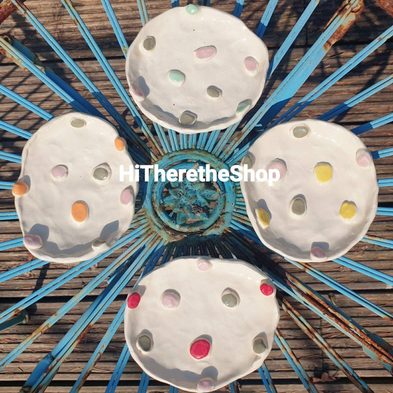 May include: Four white ceramic dishes with a raised rim and a speckled design. Each dish has a different pattern of colorful dots.
