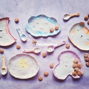 Puede incluir: Un juego de siete platos de cerámica con diseños caprichosos, que incluyen una luna, una nube, un sol y un gato. Los platos están decorados con detalles pintados a mano y tienen una gama de colores rosa claro, azul y amarillo. Los platos son perfectos para servir aperitivos o postres.