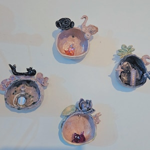 May include: Four small ceramic wall planters with different animal and nature motifs. Each planter is a sphere with a small opening at the top. The planters are painted in shades of pink, black, and green.