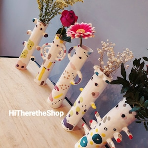 May include: Five colorful ceramic vases with abstract patterns and different shapes. The vases are filled with flowers, including white baby's breath, pink roses, and a white and pink flower.