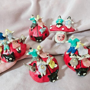 K&ouml;nnte beinhalten: Ein Set aus sechs handbemalten Keramik-Marienk&auml;fer-Figuren, jede mit einer anderen Gruppe von Menschen, die darauf reiten. Die Marienk&auml;fer sind rot mit schwarzen Punkten und haben schwarze F&uuml;hler. Die Menschen sind in verschiedenen Farben bemalt und haben unterschiedliche Gesichtsausdr&uuml;cke.