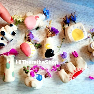 May include: A collection of small, hand-painted ceramic vases with various designs, including a sun, moon, and polka dots. The vases are filled with small bouquets of wildflowers.