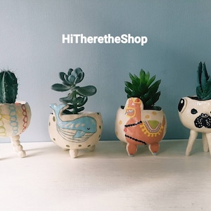 Peut inclure: Quatre pots en céramique avec différents motifs d'animaux et des pieds. Les pots sont remplis de succulentes et de cactus. Les pots sont blancs avec des motifs colorés. Le texte "HiThereTheShop" est visible en arrière-plan.