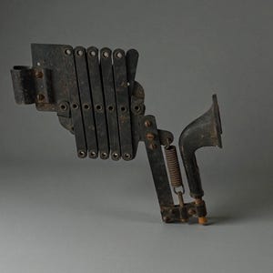 Peut inclure: Un objet métallique noir ancien avec un mécanisme en forme d'accordéon, un ressort et une extrémité en forme de corne. L'objet semble être un outil vintage ou une partie d'une machine plus grande, avec des signes visibles d'âge et d'usure.