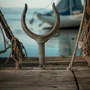 May include: A weathered metal boat cleat, shaped like a U, is mounted on a wooden dock. The cleat is a nautical hardware item used to secure ropes or lines.