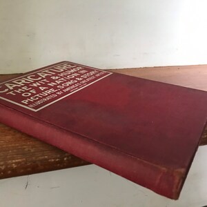 May include: A red book titled "Caricature: The Wit & Humor of a Nation in Picture, Song & Story" with silver lettering. The book is illustrated by America's Greatest Artists.