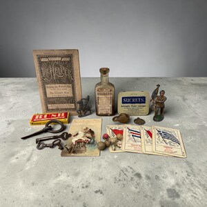 Könnte beinhalten: Eine Sammlung von Vintage-Objekten, darunter ein Buch mit dem Titel The Helper, eine Flasche mit der Aufschrift Sweet Tincture Rhubarb, eine Sucrets-Dose, drei Metallschlüssel, eine kleine Metallpferd-Figur, eine Soldatenfigur, eine Postkarte und vier Spielkarten.