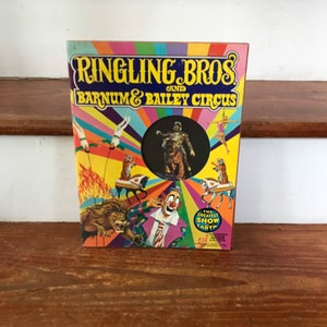 Peut inclure: Un livre vintage du cirque Ringling Bros. et Barnum & Bailey avec une couverture colorée représentant un lion, un clown et un maître de cérémonie. Le texte sur la couverture indique "Ringling Bros. et Barnum & Bailey Circus" et "The Greatest Show on Earth".