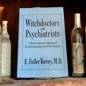 May include: A blue hardcover book titled "Witchdoctors and Psychiatrists: The Common Roots of Psychotherapy and Its Future" by E. Fuller Torrey, M.D.