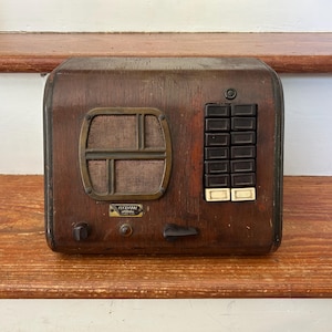 May include: A vintage wooden intercom unit with a dark brown finish, featuring a rectangular speaker grille with a brass-toned frame, a vertical column of ten black rectangular push buttons, two small knobs, and a metal label reading Flexifone.