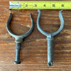 May include: Two metal boat cleat hooks with a u-shaped top and a long, thin stem. The hooks are silver in color and have a worn, weathered look.