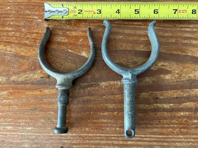 May include: Two metal boat cleat hooks with a u-shaped top and a long, thin stem. The hooks are silver in color and have a worn, weathered look.