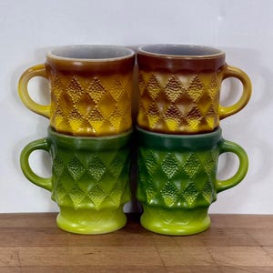 May include: A set of four glass mugs arranged in a two-by-two stack. The top two mugs feature a gradient from brown to yellow, while the bottom two mugs feature a gradient from dark green to light green. Each mug has a textured diamond pattern.