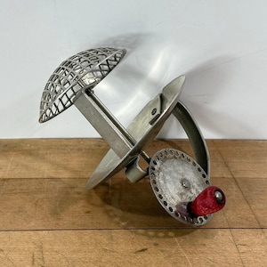 May include: A vintage, silver-toned potato ricer with a grid-patterned head and a red knob. The kitchen utensil is made of metal and has a unique design, perfect for mashing potatoes or other soft foods.