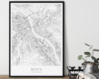 May include: Black and white city map print of Bonn, Germany, with the city name and country printed below the map. The map is framed in a black frame and is displayed on a wooden surface.