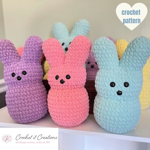 May include: Five crocheted bunny plushies in different pastel colors, including purple, pink, blue, yellow, and light blue. The plushies are arranged on a white shelf. The text "crochet pattern" is visible in a heart shape in the upper right corner of the image.