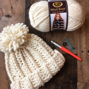 May include: A white crocheted beanie with a fluffy pom pom on top. The yarn used is Lion Brand Wool-Ease Thick & Quick.