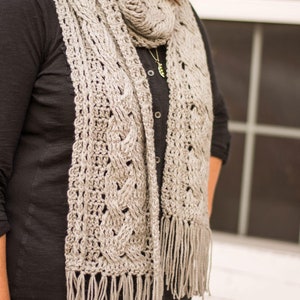 May include: A gray crocheted scarf with a fringe. The scarf is made with a delicate, openwork pattern.