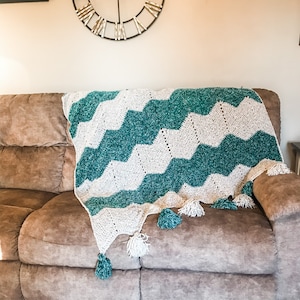 May include: A teal and white crocheted throw blanket with fringe tassels draped over a brown couch.