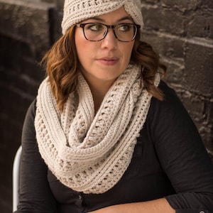 Può includere: Una donna indossa una fascia per capelli in crochet beige e una sciarpa infinita abbinata. Indossa occhiali e una camicia nera.