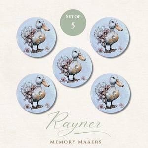 May include: A set of five round buttons, each with a duck illustration and floral accents. The duck is depicted with a bow and a silver button hole. The text "Rayner Memory Makers" is at the bottom. The background is light blue.