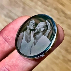 May include: A silver round pendant with a black and white engraved image of a couple laughing.