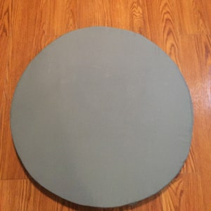 May include: A round, light gray, fabric table topper. The table topper is on a wood floor.