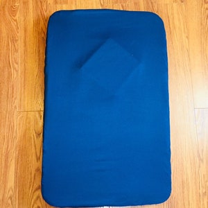 May include: A dark blue rectangular cushion or pad, likely for a chair or seat, on a wooden floor.