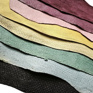 May include: A collection of layered leather sheets featuring a distinct snakeskin-like embossed texture. The stack includes pieces in black, light blue, sage green, yellow, light pink, and deep burgundy, all arranged in an overlapping diagonal pattern.