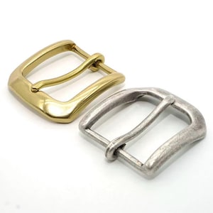 Peut inclure: Deux boucles de ceinture en métal. L'une est de couleur or brillant, l'autre de couleur argent mat. Les deux ont une forme carrée avec une barre arrondie pour la sangle de ceinture.