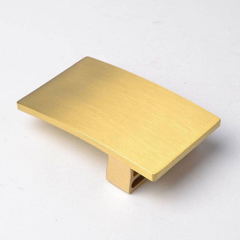 K&ouml;nnte beinhalten: Eine geb&uuml;rstete goldene G&uuml;rtelschnalle mit rechteckiger Form und leicht gekr&uuml;mmtem Design.