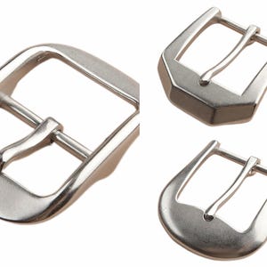 May include: Three silver belt buckles are shown against a white backdrop. The buckles, in various shapes, are made of shiny metal and feature a classic design with a single prong.