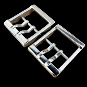 Puede incluir: Dos hebillas de cinturón de metal plateado con un diseño texturizado único. Las hebillas tienen forma rectangular y un acabado liso y pulido.