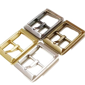 May include: Four metal belt buckles in different finishes: silver, gold, brass, and nickel. The buckles are all the same size and shape, with a rectangular frame and a center bar with a small loop.