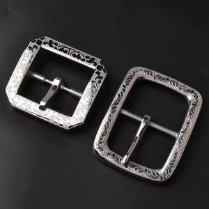 May include: Two silver belt buckles with an ornate floral design. The buckles are rectangular and have a polished finish.
