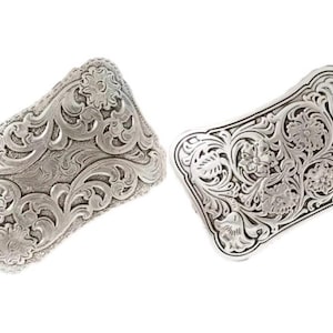 May include: Two silver-colored rectangular belt buckles with intricate floral and scrollwork designs. The buckles have a detailed, embossed appearance, showcasing a classic Western aesthetic. The buckles are displayed against a white background.