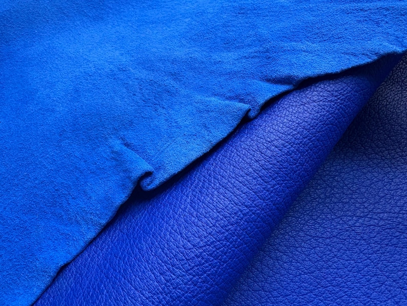 May include: Close-up of two pieces of blue leather. The top piece is a vibrant, textured suede, while the bottom piece is a smooth, pebbled leather. The colors are a deep, rich blue, creating a striking contrast.