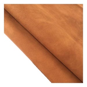 Puede incluir: Primer plano de un trozo de cuero doblado de color marrón claro. El cuero tiene una superficie texturizada y parece suave y flexible. Los pliegues crean sombras y reflejos, añadiendo profundidad a la imagen. El cuero se utiliza probablemente para la artesanía.