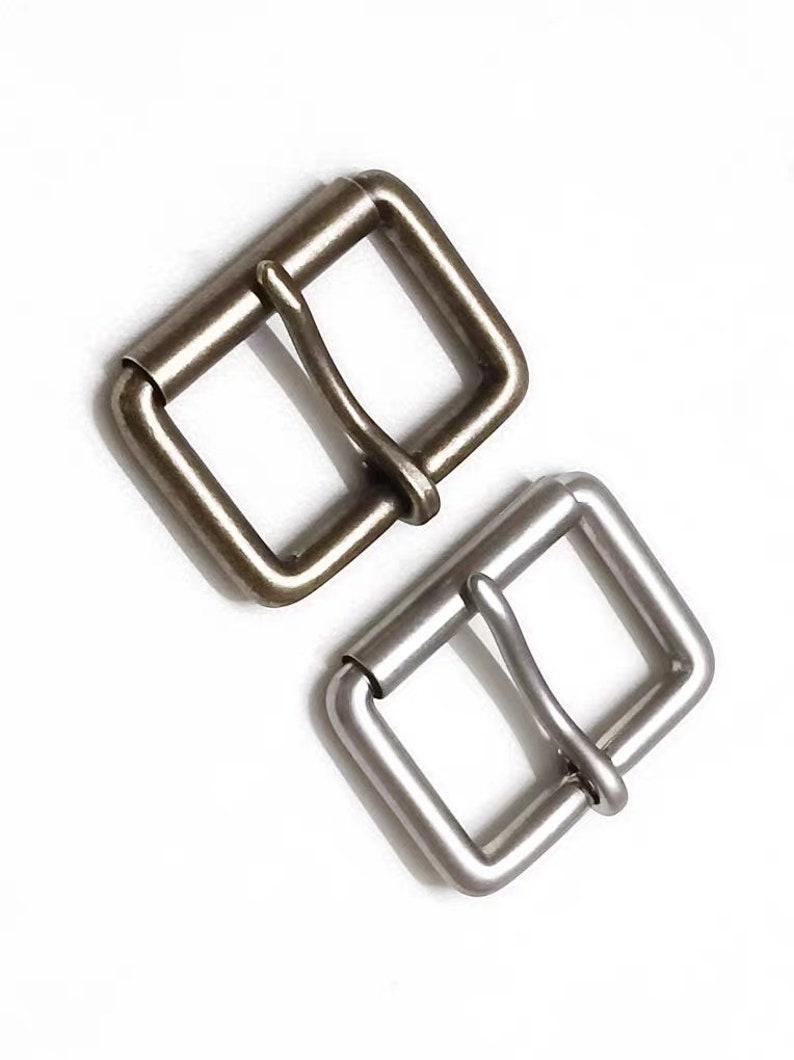 May include: Two metal belt buckles, one antique brass and one silver, both with a square shape and a single prong.