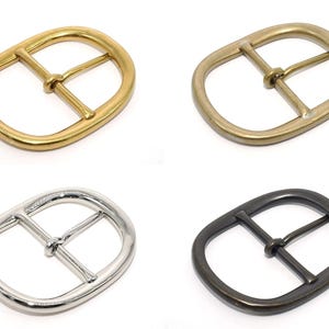 May include: Four metal belt buckles in different finishes: gold, brass, silver, and black. Each buckle has a classic oval shape with a center bar.