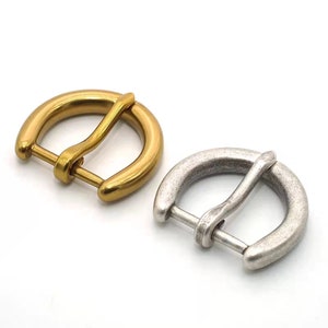 May include: Two metal belt buckles, one gold and one silver, with a D-ring design. The buckles are both about 1 inch in diameter.