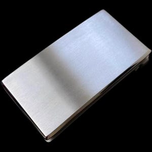 Puede incluir: Un clip para dinero de plata con acabado cepillado. El clip es rectangular y tiene una superficie lisa y elegante.
