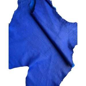 May include: A piece of vibrant blue leather with a textured surface. The leather is irregularly shaped with torn edges, revealing a lighter blue underside. The material is likely used for crafting.