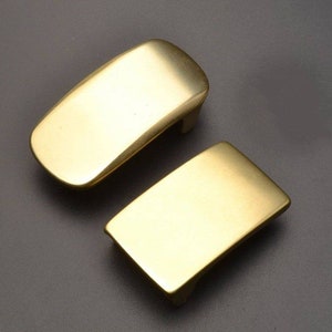 May include: Two gold-colored metal belt buckles. One buckle is rectangular and the other is curved.