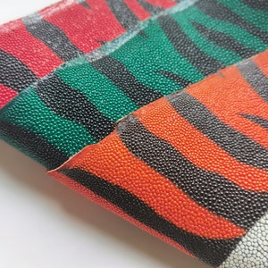 Puede incluir: Primer plano de cuero texturizado en rojo, verde y naranja con patrones de rayas negras. El cuero tiene una superficie rugosa y punteada. El diseño recuerda a un patrón de cebra. El material está doblado, revelando la parte inferior.