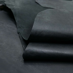 May include: Close-up of a stack of black leather hides. The leather has a smooth, textured surface.