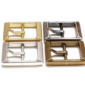 Pu&ograve; includere: Quattro fibbie per cintura in metallo in diverse finiture: oro, argento, nero e ottone. Ogni fibbia &egrave; rettangolare con una superficie liscia e un solo perno.