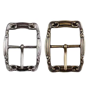 Può includere: Due fibbie per cintura in metallo ornate. Una è color argento, l'altra color oro. Entrambe hanno una forma rettangolare con decorazioni a volute e una barra centrale per il cinturino.